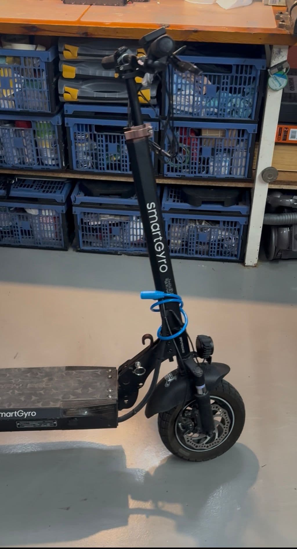 Patinete electrico SmartGyro negro en el taller con candado azul en el tubo